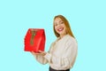 Portrait of a beautiful cute red-haired girl holding a gift box of a red color with a green velvet ribbon lifting the Royalty Free Stock Photo