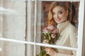 Portrait of a beautiful delicate blonde smiling girl with roses, standing outside the window. Royalty Free Stock Photo