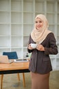 A beautiful Muslim businesswoman stands in her modern office with a coffee cup in her hands Royalty Free Stock Photo