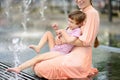 Portrait of beautiful disabled girl in the arms of his mother having fun on fountain of public park at sunny summer day. Child Royalty Free Stock Photo