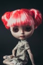 Portrait of a beautiful doll, sitting, pink hair, gray shirt. Black background.