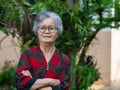 Portrait of a beautiful elderly Asian woman smiling and arms crossed while standing in a garden Royalty Free Stock Photo