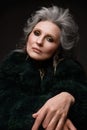 Portrait of a beautiful elderly woman in a leopard blouse and fur coat with classic makeup and gray hair.
