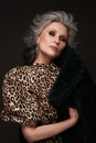 Portrait of a beautiful elderly woman in a leopard blouse and fur coat with classic makeup and gray hair.