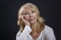 Portrait of a beautiful elderly woman. A smiling blonde sits with her hand resting her cheek. Happy maturity. Close-up. Black Royalty Free Stock Photo