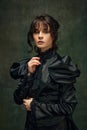 Portrait of beautiful, elegant young woman in Victorian black dress standing against dark vintage green textured