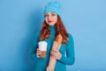 Portrait of beautiful european red haired woman wearing casual sweater and cap, holding coffee to go and long loaf in hands, wears Royalty Free Stock Photo