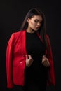 Portrait of a beautiful fashionable brunette woman in a red business suit on black background Royalty Free Stock Photo