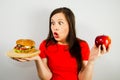 Portrait of a beautiful fat girl in surprise and holding a red apple and a hamburger, on gray background