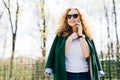 Portrait of beautiful female with fluffy blonde hair talking on cell phone to her friend, looking happily and excited standing aga Royalty Free Stock Photo