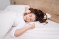 Young woman sleeping in bed. Portrait of beautiful female resting on comfortable bed with pillows In white bedding In light Royalty Free Stock Photo