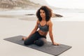 Portrait of a beautiful female sitting on a mat on beach. Woman relaxing after yoga exercises at sunset looking at camera Royalty Free Stock Photo