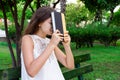 Portrait of a beautiful female student who is tired of studying is sitting on a bench outside and holding a book Royalty Free Stock Photo