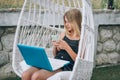 Beautiful girl sitting in garden chair, using laptop and smartphone Royalty Free Stock Photo