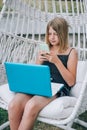 Beautiful girl sitting on swing chair, using laptop and smartphone Royalty Free Stock Photo