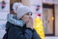 Portrait of a beautiful forty-year-old woman warming her frozen hands with her breath on the street against the backdrop of city N