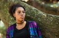 Portrait of a beautiful freckled face brown skin young woman besides a mossy tree trunk