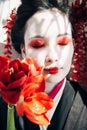 Beautiful geisha holding red flowers in sunlight