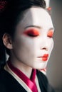 Beautiful geisha with red and white makeup with closed eyes in sunlight