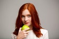 Portrait of beautiful ginger girl holding apple over gray background. Royalty Free Stock Photo