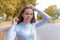 Portrait of beautiful girl autumn in city, background trees leaves on ground. Happy smiling straightens her hair Royalty Free Stock Photo