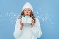 Portrait of a beautiful girl blowing snow off a gift over an isolated blue background. Snow flies into the camera