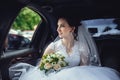 Portrait of a beautiful girl in the car. The bride holds a wedding bouquet in her hands and looks at the street through the car