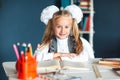 Portrait of a beautiful girl in the classroom. Little schoolgirl with white bows sitting at the table and studying. Education and Royalty Free Stock Photo