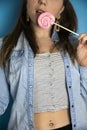 Portrait of a beautiful girl with colorful pink twirl lollipop hard candy on blue background, sweets,sugar unhealthy