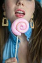 Portrait of a beautiful girl with colorful pink twirl lollipop hard candy on blue background, sweets,sugar unhealthy