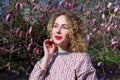 Portrait of beautiful girl with curly long hair in pink blouse walks in garden of magnolias