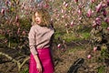Portrait of beautiful girl with curly long hair in pink blouse walks in garden of magnolias