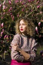 Portrait of beautiful girl with curly long hair in pink blouse walks in garden of magnolias