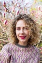 Portrait of beautiful girl with curly long hair in pink blouse walks in garden of magnolias