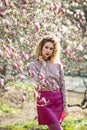 Portrait of beautiful girl with curly long hair in pink blouse walks in garden of magnolias