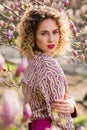 Portrait of beautiful girl with curly long hair in pink blouse walks in garden of magnolias