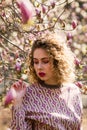 Portrait of beautiful girl with curly long hair in pink blouse walks in garden of magnolias