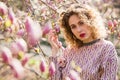 Portrait of beautiful girl with curly long hair in pink blouse walks in garden of magnolias