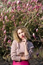 Portrait of beautiful girl with curly long hair in pink blouse walks in garden of magnolias