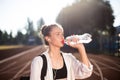 Portrait of beautiful girl in earphones drinking water on running track of stadium