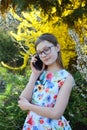 Portrait of beautiful girl with glasses and brown hair talk on smart phone. Young smiling teneeger in green spring park resting Royalty Free Stock Photo