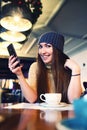 Portrait of beautiful girl in hat using her mobile phone in cafe. Tonned. Selective focus. Royalty Free Stock Photo