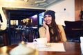 Portrait of beautiful girl in hat using her mobile phone in cafe. Tonned. Selective focus. Royalty Free Stock Photo