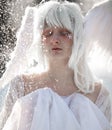 Portrait of beautiful girl in image of good angel with wings against background of snowfall