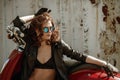 Portrait of a beautiful girl in leather jacket, brassiere and glasses near red motorcycle Royalty Free Stock Photo