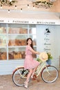 Portrait of a beautiful girl with long curly hair in a dress sitting on a yellow retro bicycle on the background of a Parisian caf