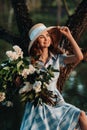 Portrait of a beautiful girl with long hair, a straw hat and a long summer dress with lilac flowers in the garden Royalty Free Stock Photo