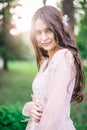 Portrait of beautiful girl on nature near the green trees in the sun, in a beige lace dress, looks with smile, closeup Royalty Free Stock Photo