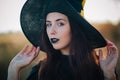 Portrait of a beautiful girl with pale skin and black lips in a big black hat. Woman in the image of a witch for Halloween. Royalty Free Stock Photo