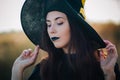 Portrait of a beautiful girl with pale skin and black lips in a big black hat. Woman in the image of a witch for Halloween. Royalty Free Stock Photo